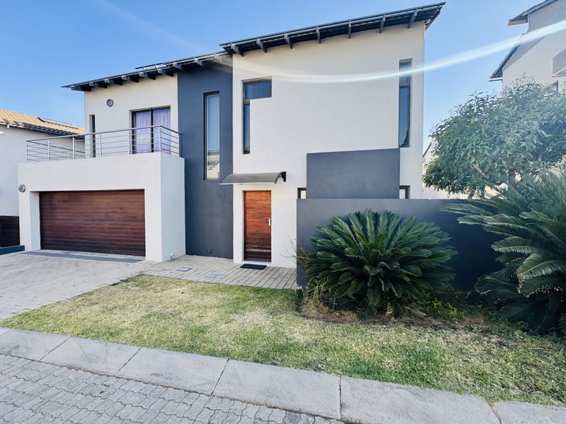 Modern double-storey home featuring a timber garage door, a private balcony with stainless steel balustrades, and a contemporary paved entrance.