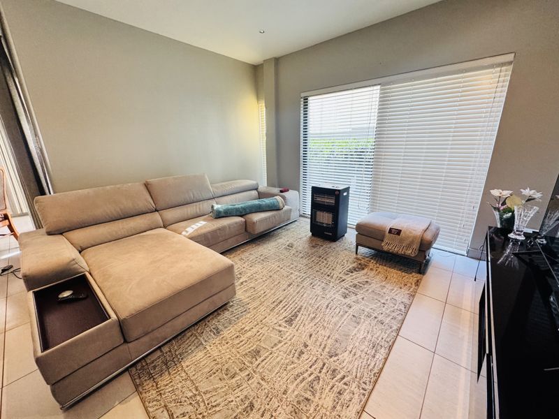 A well-lit living room featuring tiled flooring and a large sliding glass door with venetian blinds, providing access to the exterior.