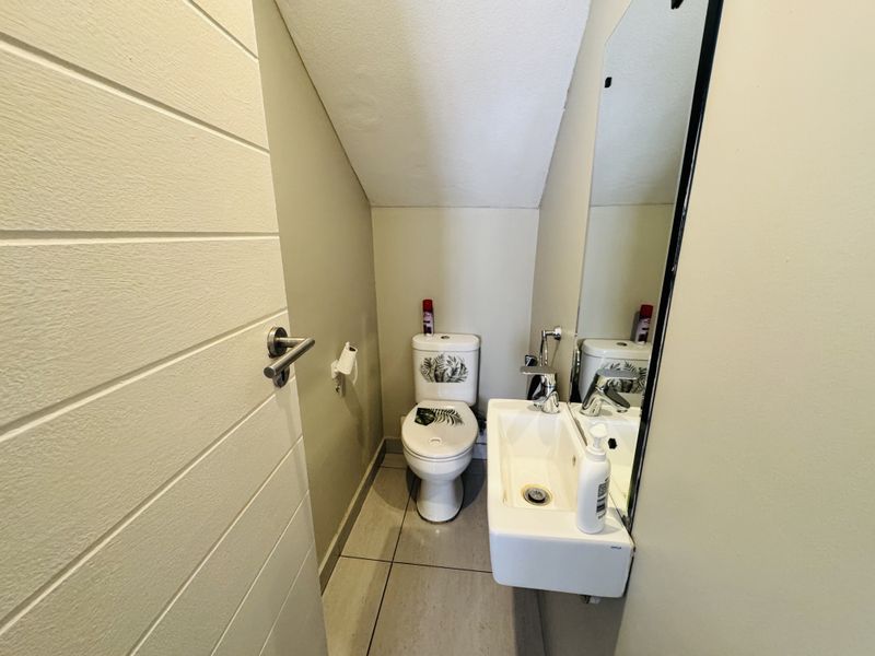 A compact guest cloakroom featuring a wall-mounted basin, modern mixer tap, and a toilet, finished with neutral wall paint and tiled flooring.