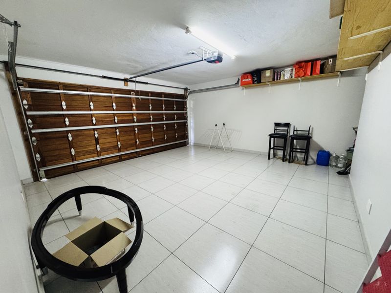A spacious, clean garage featuring tiled flooring, a sectional wooden garage door, and built-in wall shelving for storage.