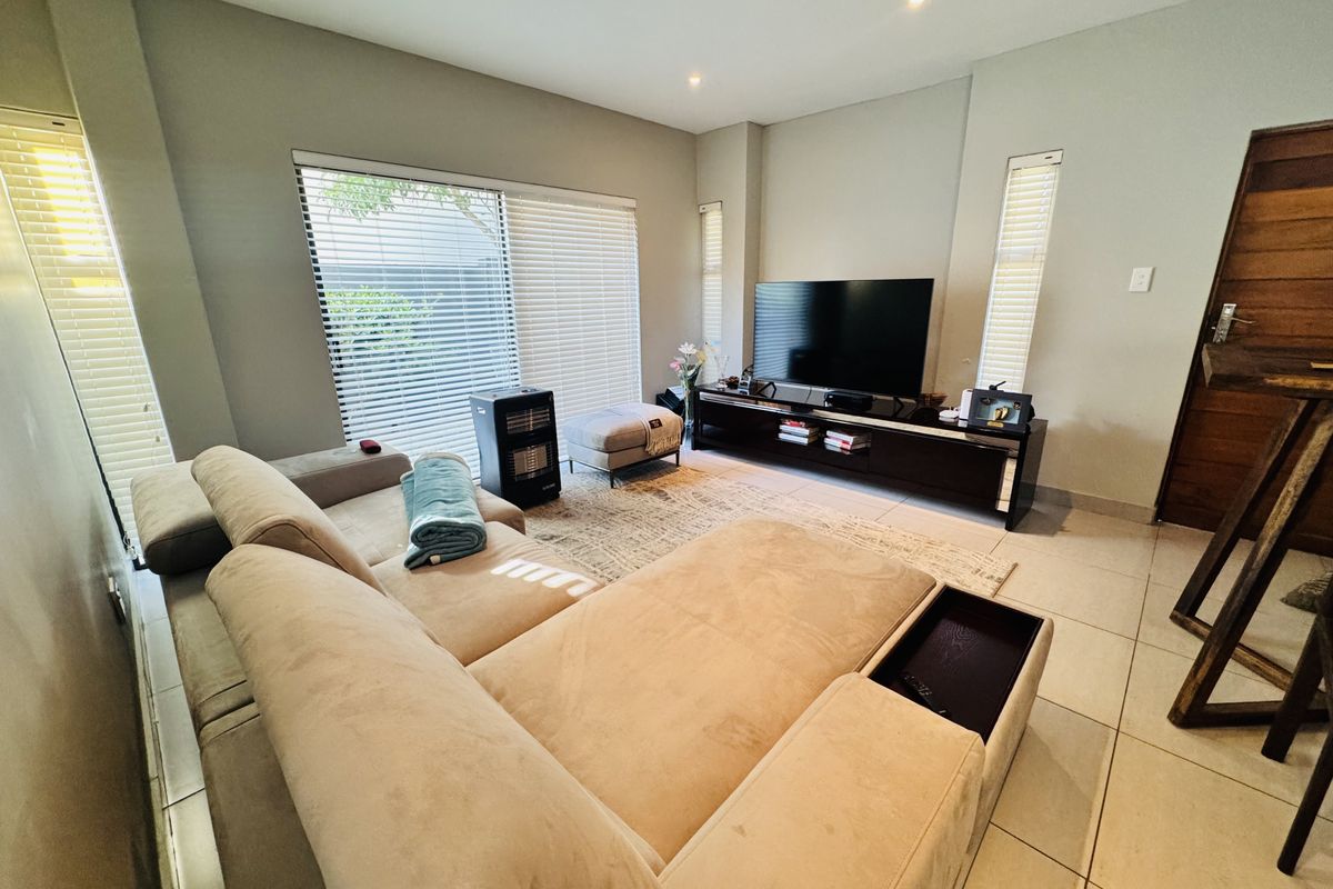 A well-maintained living room featuring tiled flooring, recessed downlights, and a large sliding glass door with venetian blinds providing access to the exterior.