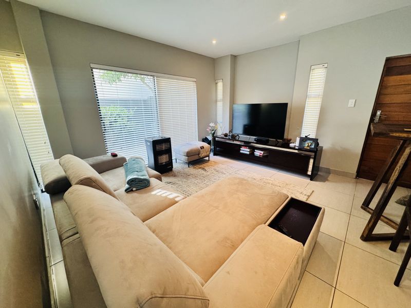 A well-maintained living room featuring tiled flooring, recessed downlights, and a large sliding glass door with venetian blinds providing access to the exterior.