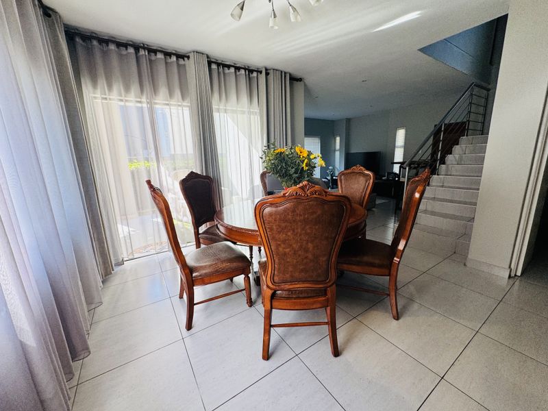 A bright dining area featuring large sliding glass doors, neutral tiled flooring, and an open-plan staircase with a modern metal railing.