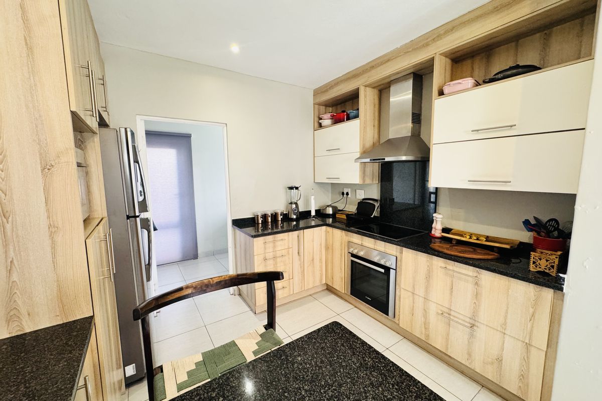 Modern kitchen featuring light wood-grain cabinetry, dark granite countertops, stainless steel appliances, and tiled flooring with a functional layout.