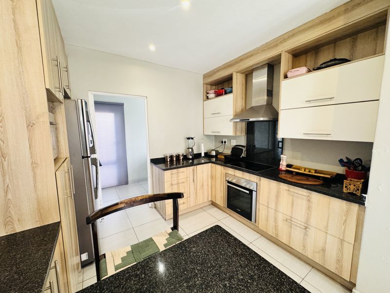 Modern kitchen featuring light wood-grain cabinetry, dark granite countertops, stainless steel appliances, and tiled flooring with a functional layout.