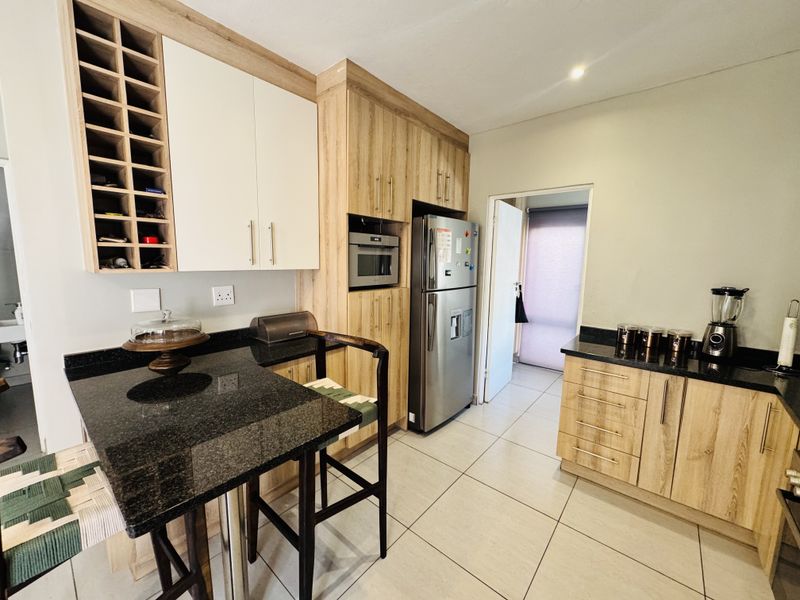 Modern kitchen featuring light wood-tone cabinetry, contrasting black granite countertops, built-in microwave, and integrated wine storage with tiled flooring.