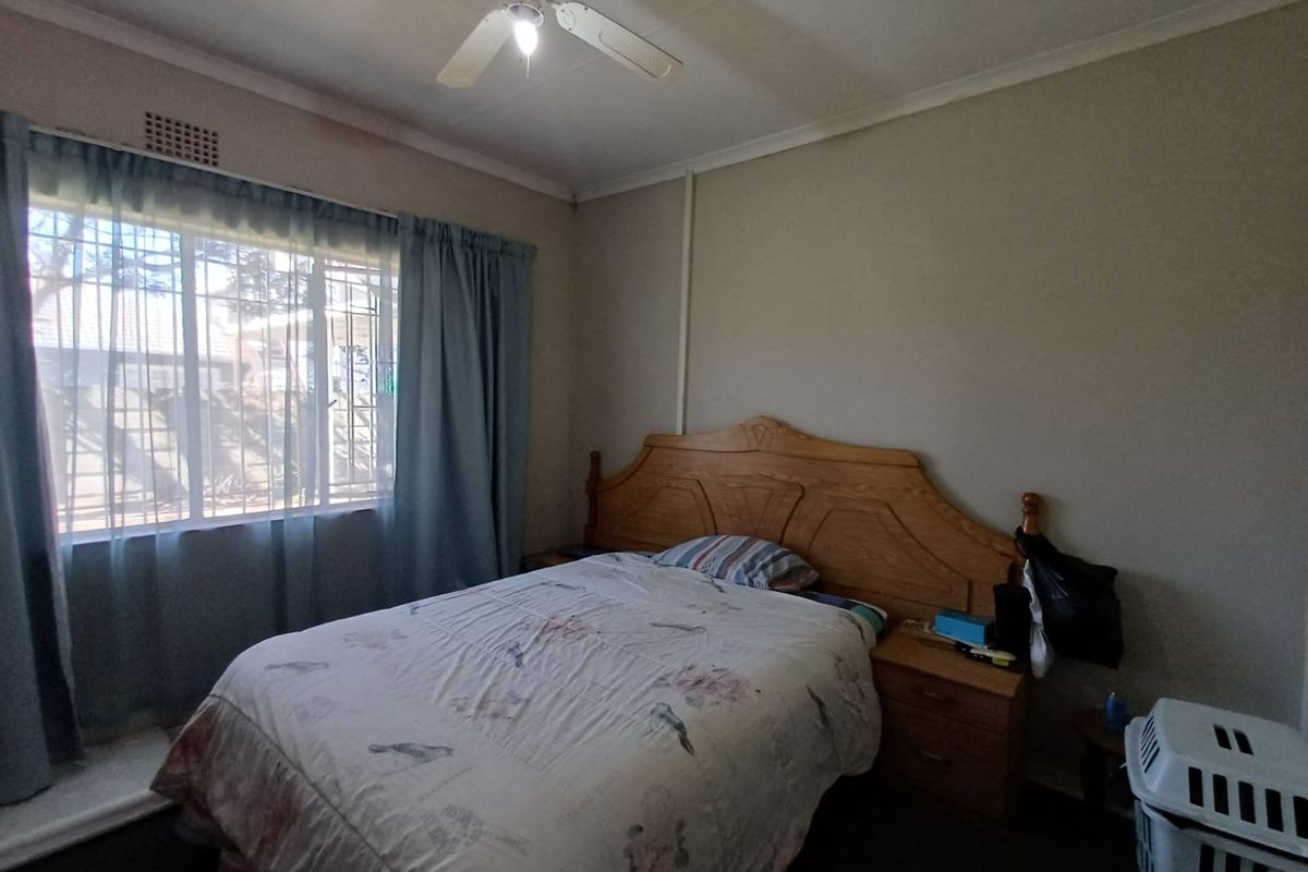 A standard bedroom featuring a ceiling fan, security bars on the window, and neutral wall finishes.