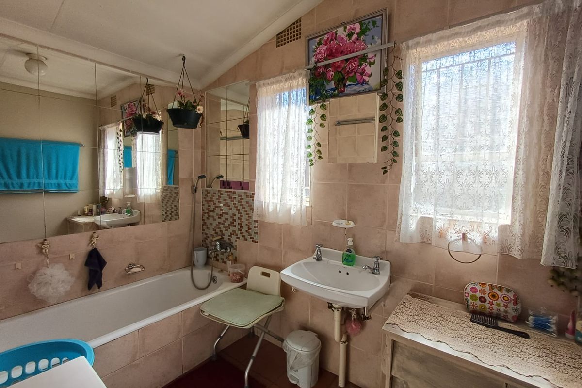 A dated bathroom featuring a built-in bathtub, wall-mounted basin, and full-height wall tiling, offering potential for a modern renovation.