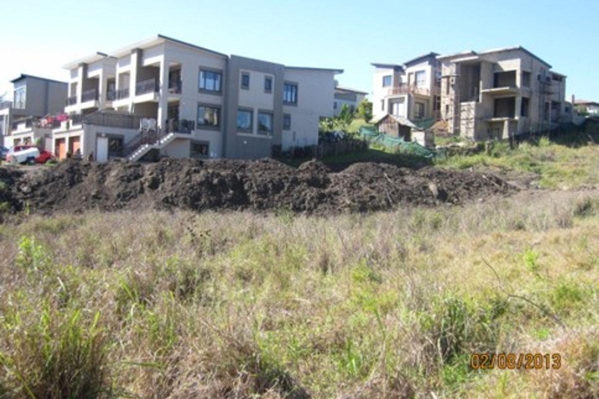 A view of a vacant residential plot with sloped terrain, situated in a developed neighborhood with surrounding multi-story residential properties.