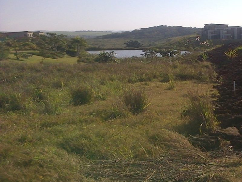 A scenic view of the vacant residential land overlooking a natural landscape, water body, and surrounding estate greenery.