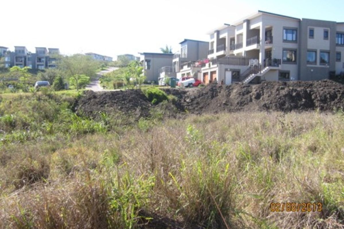 A view of a vacant residential plot featuring sloped terrain and an embankment, situated in a developed estate setting.