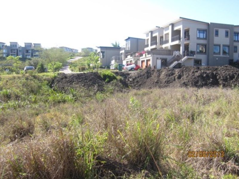 A view of a vacant residential plot featuring sloped terrain and an embankment, situated in a developed estate setting.