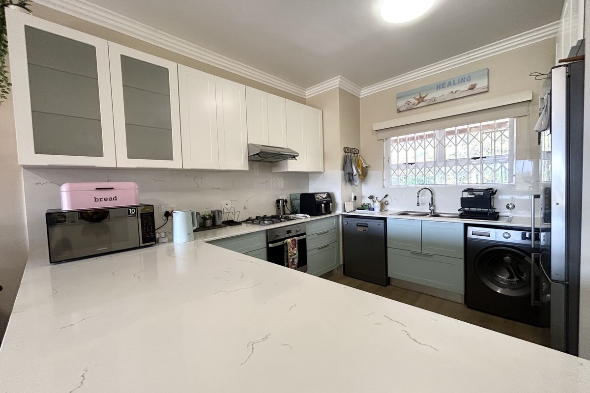 Modern kitchen featuring white quartz countertops, two-tone cabinetry, built-in oven with gas hob, extractor fan, and integrated dishwasher with a window overlooking the exterior.
