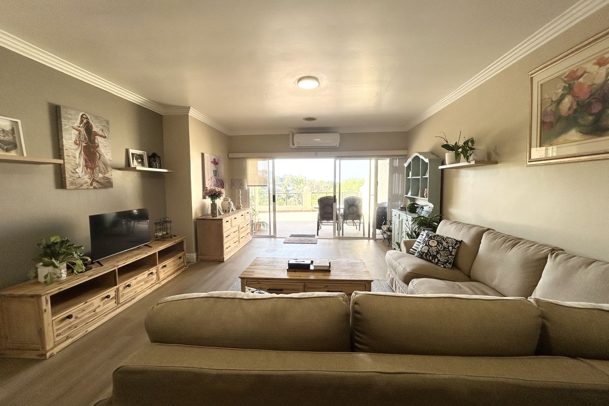 Spacious living room featuring neutral walls, crown molding, laminate flooring, and a split-system air conditioner, with direct access to an outdoor balcony.