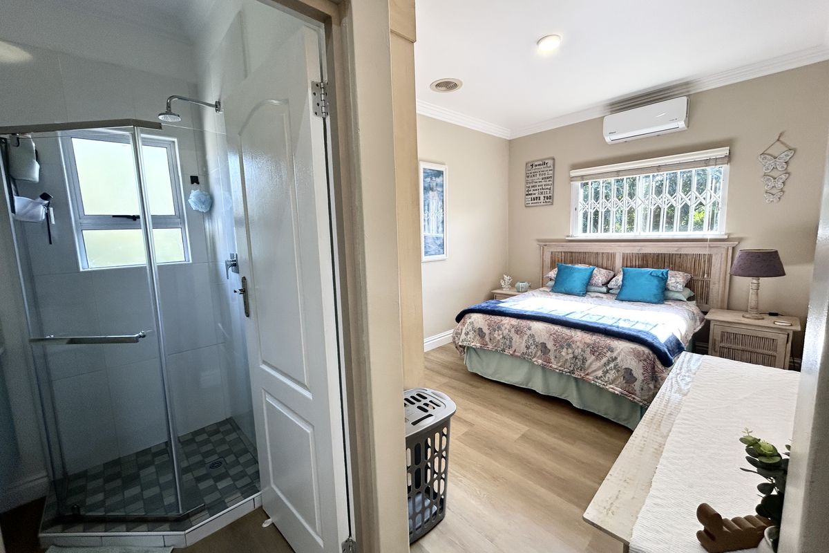 A well-maintained bedroom featuring laminate flooring, an en-suite shower, and a wall-mounted split-system air conditioner for climate control.