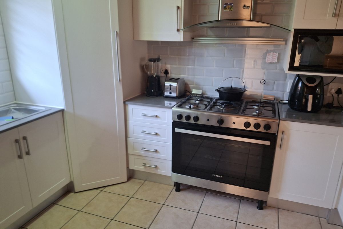 A functional kitchen featuring white cabinetry, stone countertops, a gas stove with extractor fan, and a subway tile backsplash.