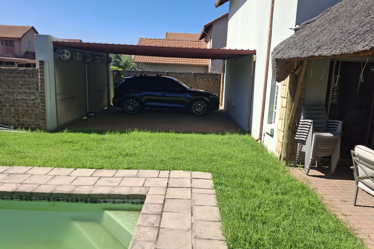 Rear exterior view featuring a swimming pool, paved patio area, and a covered carport structure adjacent to the main dwelling.