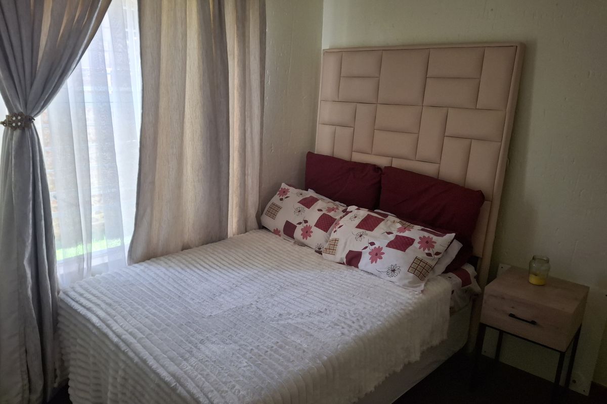 A cozy bedroom featuring a neutral color palette, large window with curtains, and space for a double bed.