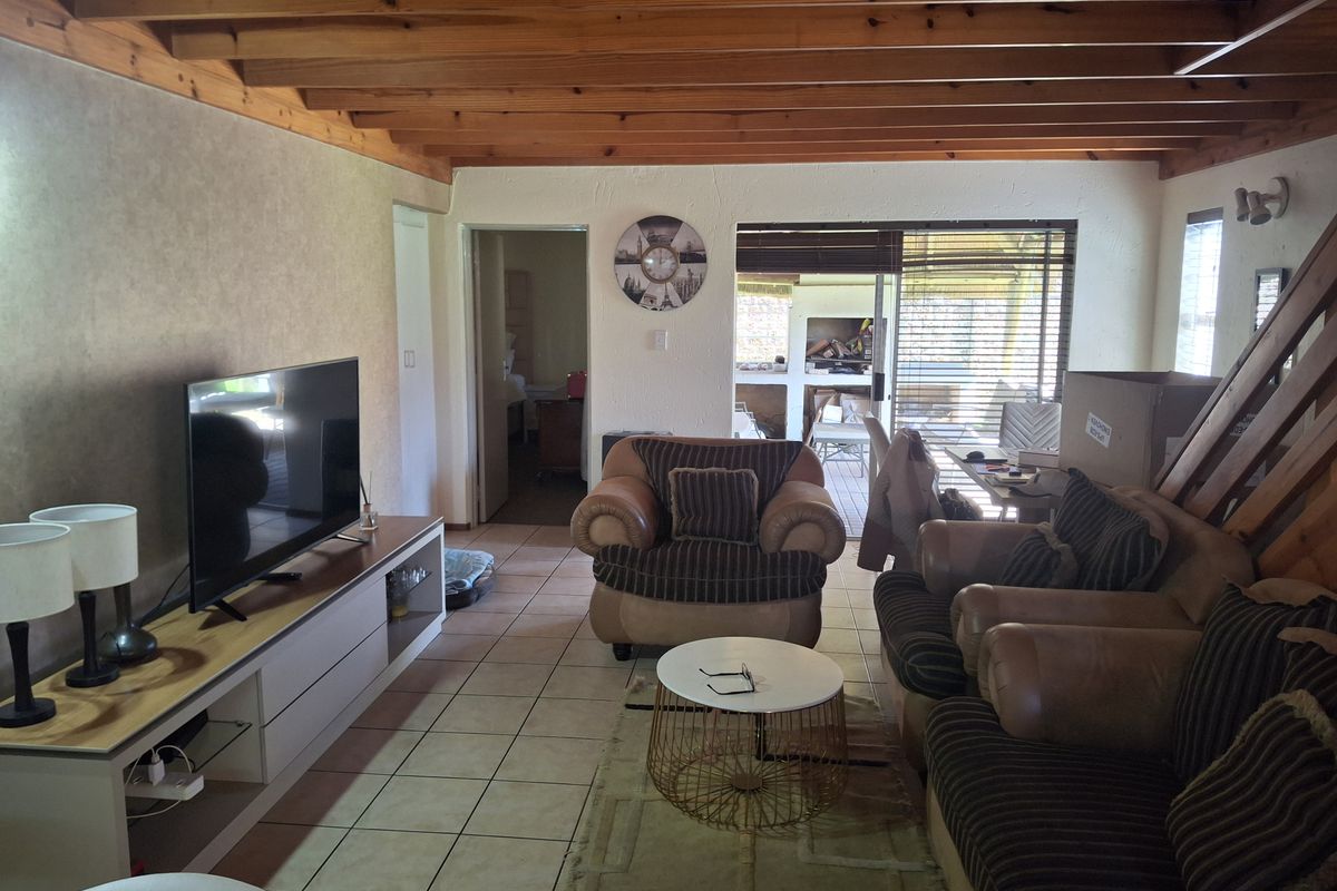 Spacious living room featuring exposed timber beam ceilings, ceramic floor tiles, and direct access to an outdoor patio area through sliding glass doors.