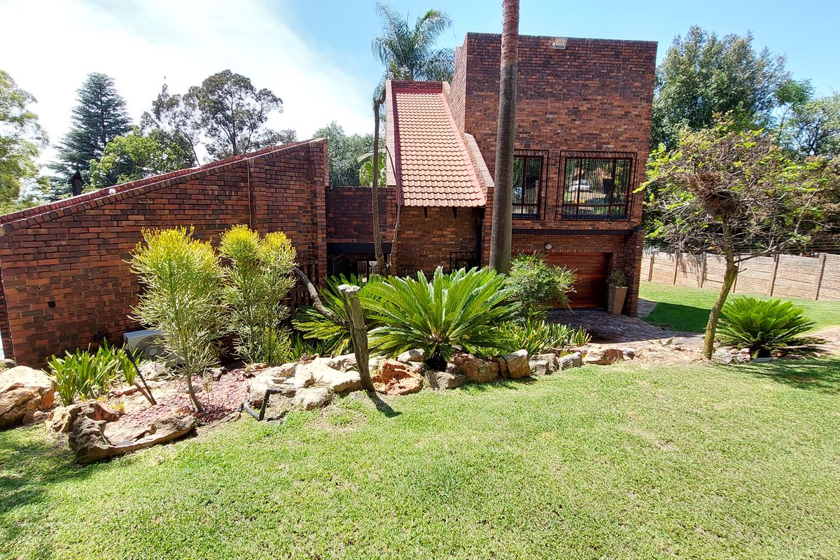 A rear view of a face-brick house featuring a landscaped garden, rockery, and secure garage access.