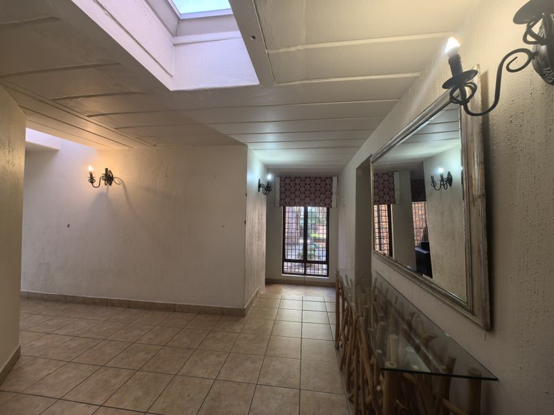 Spacious hallway featuring tiled flooring, a skylight providing natural light, and wall-mounted lighting fixtures.
