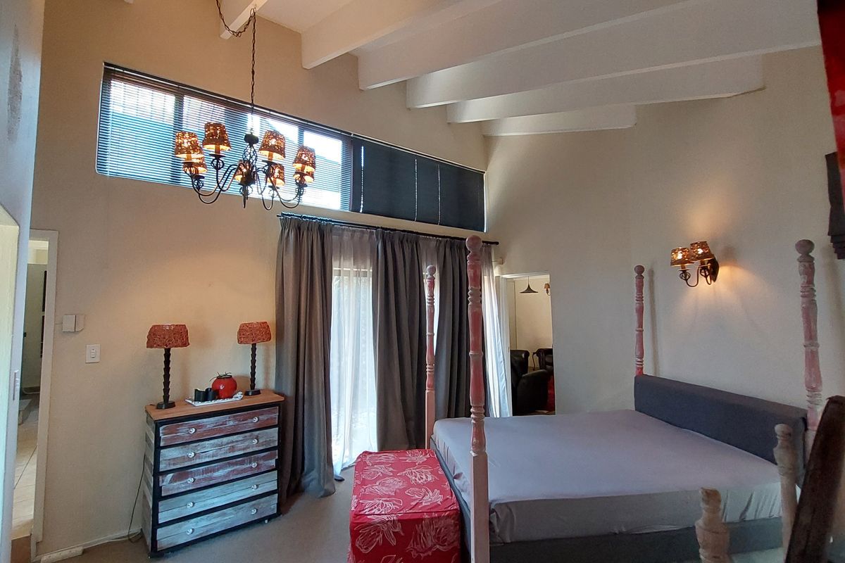 Spacious bedroom featuring high vaulted ceilings with exposed beams, clerestory windows for natural light, and direct access to the outdoors via sliding glass doors.