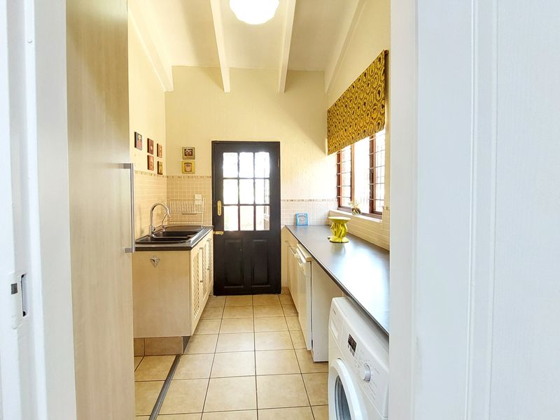 Functional laundry room featuring tiled flooring, built-in cabinetry with laminate countertops, a double sink, and direct access to the exterior.