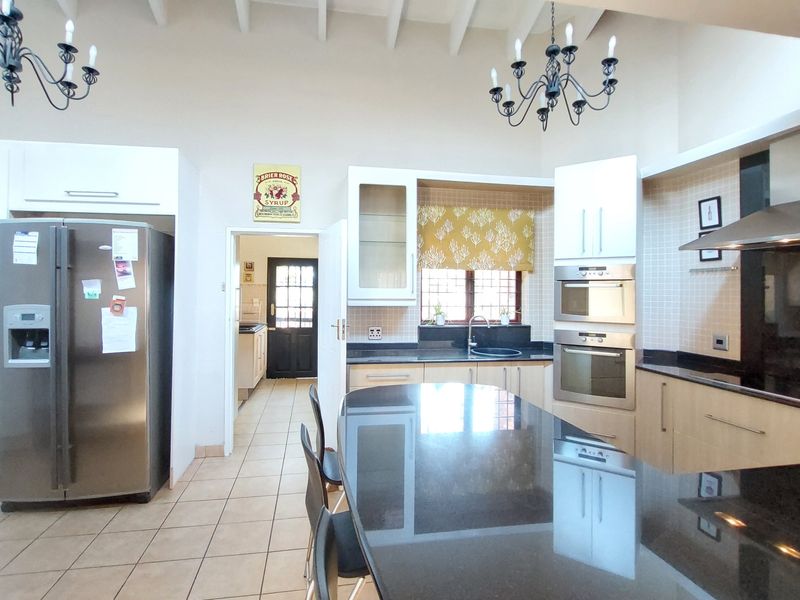 Spacious kitchen featuring granite countertops, a central island, built-in appliances, and high ceilings with exposed beams, leading to a separate scullery area.
