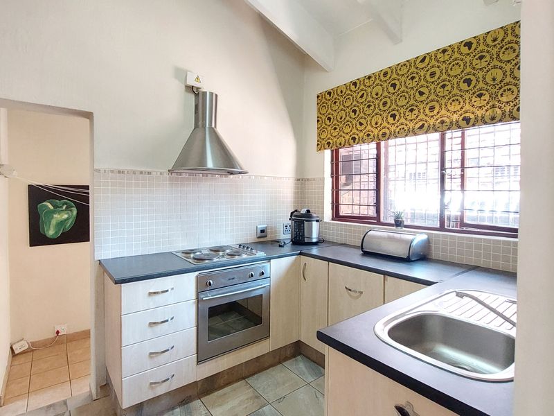 Functional kitchen featuring light-toned cabinetry, dark laminate countertops, built-in oven with extractor fan, tiled splashback, and a stainless steel sink.