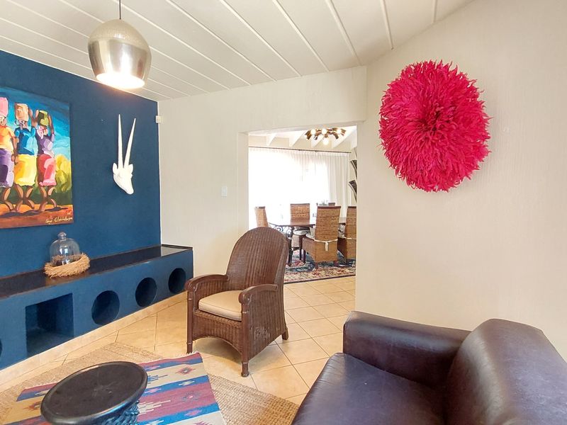 A living room featuring a built-in blue display unit, tiled flooring, and a tongue and groove ceiling, with an open transition to the dining area.