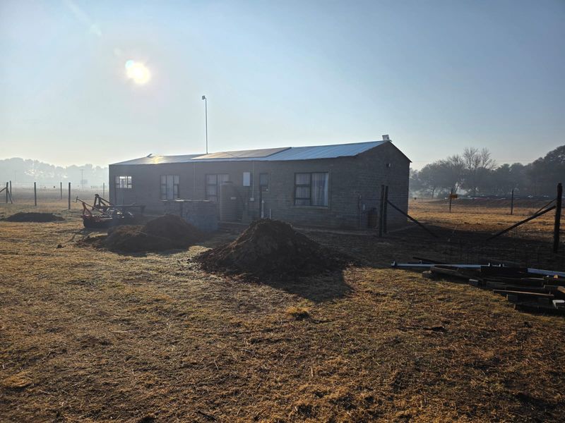 Rear view of a brick dwelling featuring a metal roof with solar panels, a water tank, and surrounding undeveloped land.