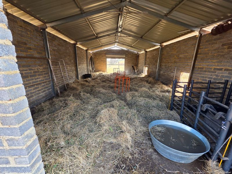 A functional utility barn or livestock shelter featuring exposed brick walls, a corrugated metal roof, and a steel frame structure.