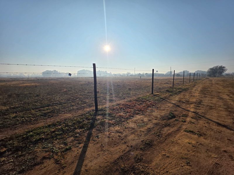 A wide, open plot of land featuring a perimeter barbed wire fence and an unpaved dirt access track.