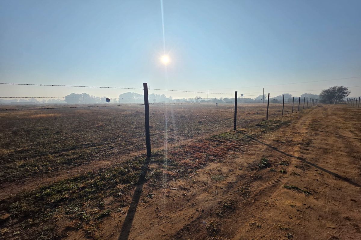 A wide, open plot of land featuring a perimeter barbed wire fence and an unpaved dirt access track.