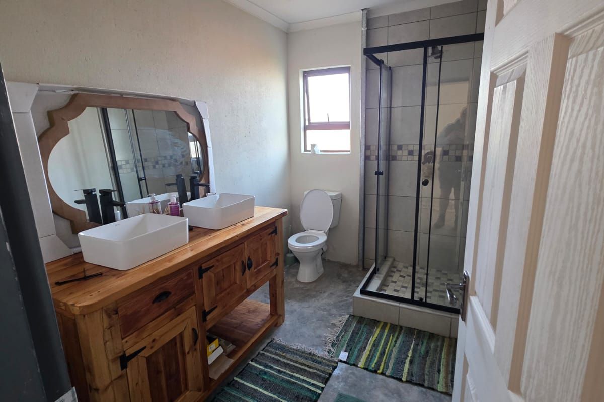 Modern bathroom featuring a double vanity with vessel sinks, a glass-enclosed shower, and a toilet, finished with concrete-style flooring.