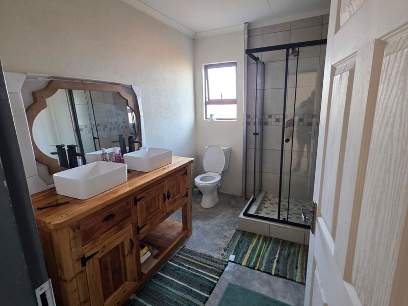 Modern bathroom featuring a double vanity with vessel sinks, a glass-enclosed shower, and a toilet, finished with concrete-style flooring.
