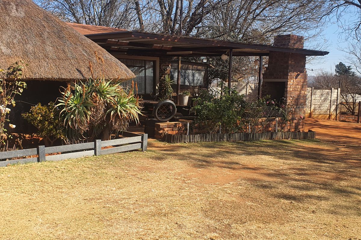Rear view of a small holding property featuring a thatched roof dwelling, a covered patio with a built-in brick fireplace, and surrounding garden space.