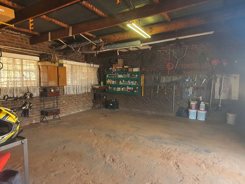A functional garage space featuring exposed brick walls, timber roof trusses, and a concrete floor, currently utilized for storage and workshop purposes.