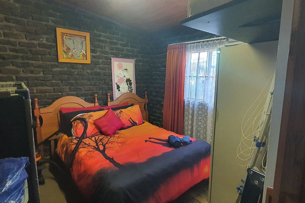 A bedroom featuring exposed brick walls and a timber ceiling, providing a rustic aesthetic with natural light through a window with security bars.