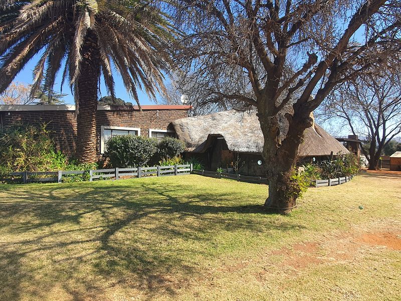 Front view of a facebrick small holding property featuring a traditional thatch roof, established garden, and perimeter fencing.