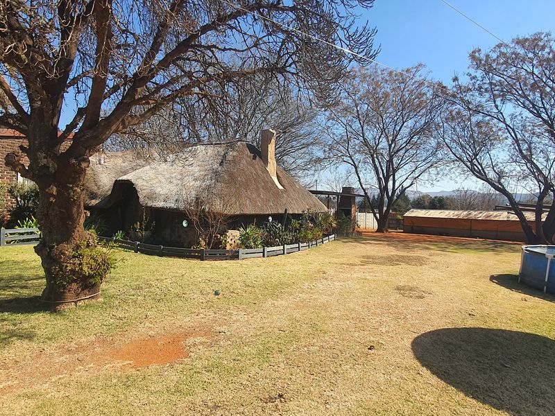 Rear garden view featuring a traditional thatch-roofed structure, mature trees, and a swimming pool set within a spacious, established outdoor area.