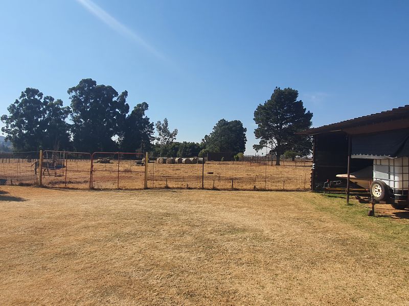 A wide view of the rear small holding grounds featuring a large open field, wire fencing, and a covered storage or utility structure.