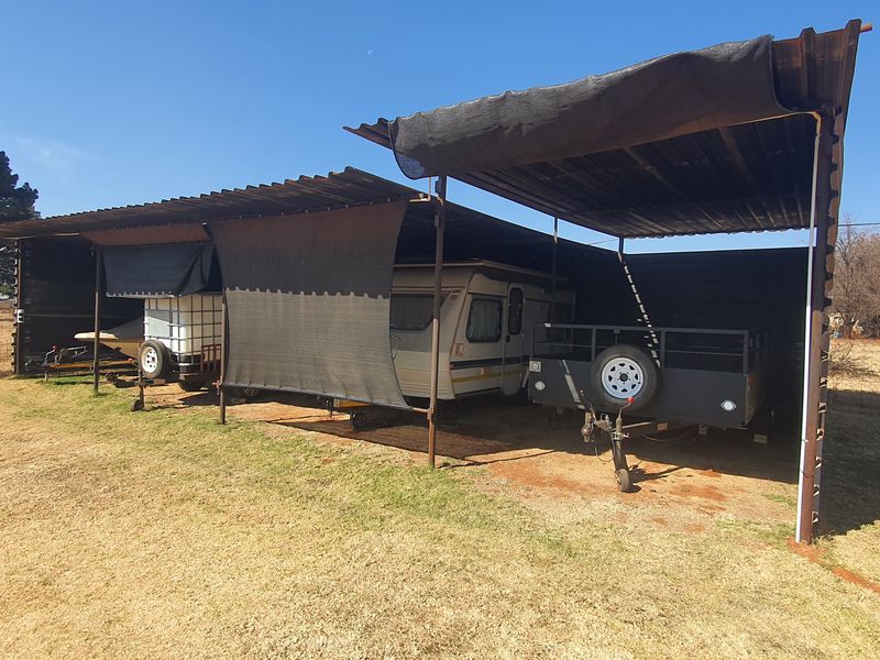 Open-sided corrugated iron carport structure providing covered storage for vehicles and trailers on the small holding.