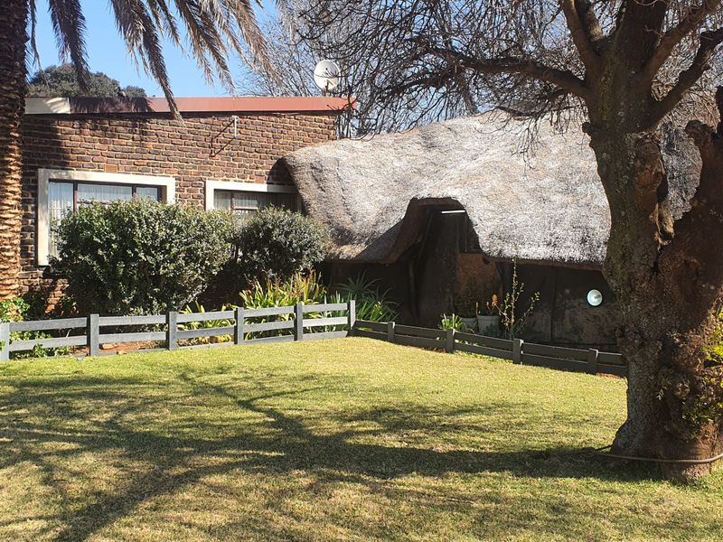 Front view of a small holding property featuring a traditional thatched roof section and face brick exterior with a surrounding timber fence.