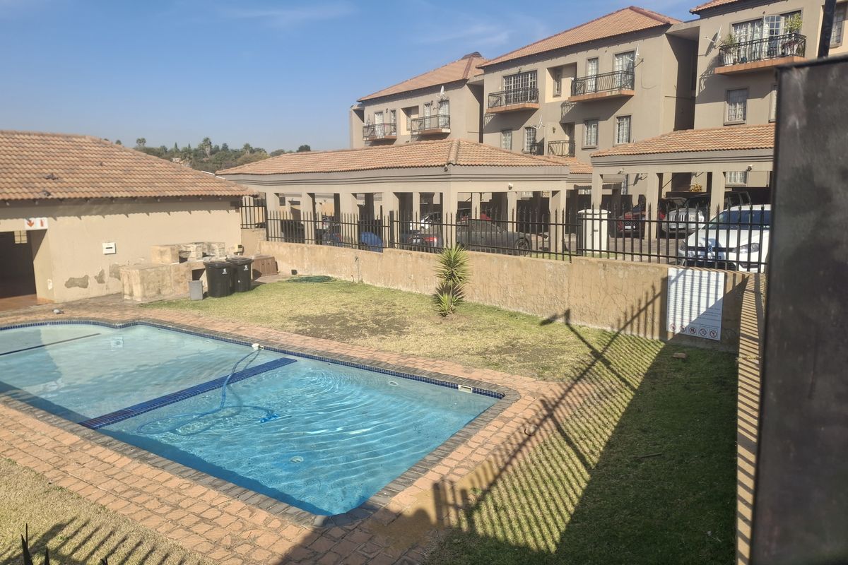 A communal pool area within a cluster complex, featuring a swimming pool, brick paving, and a built-in braai area set against multi-story residential units.