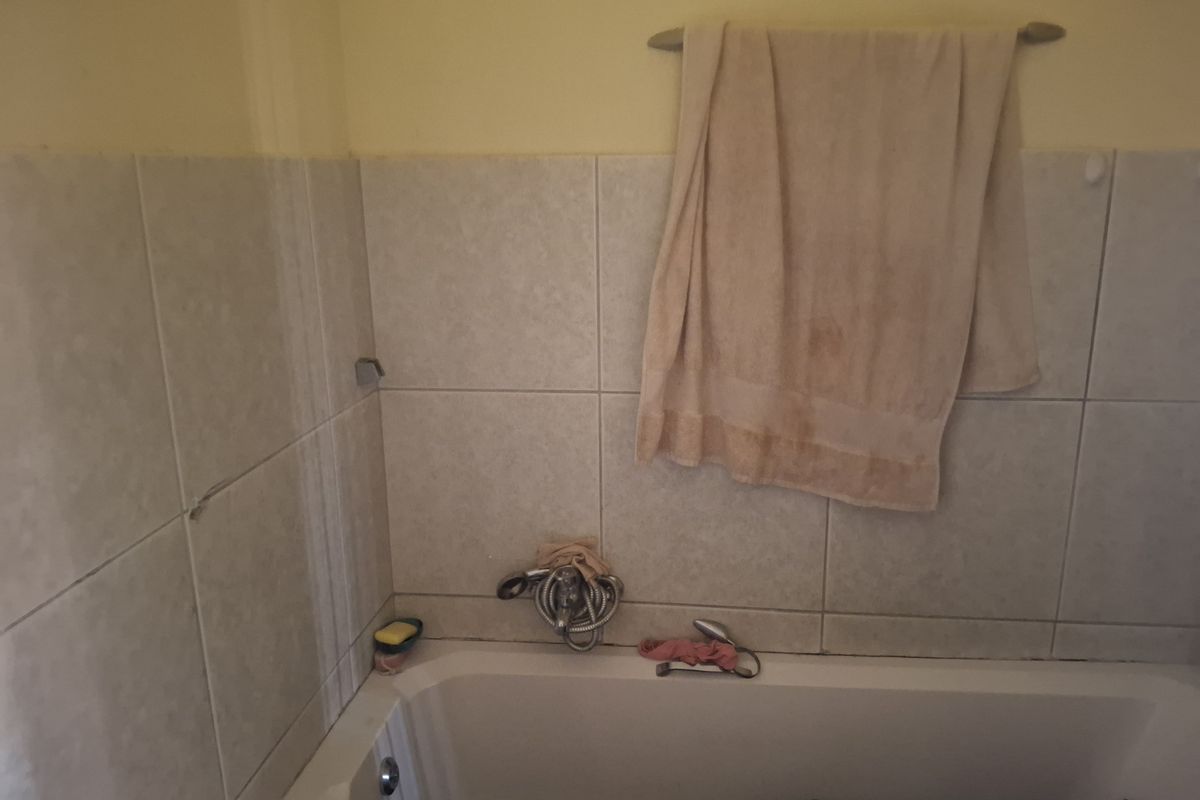 A bathroom featuring a built-in bathtub with wall-mounted shower mixer and tiled splashback area.