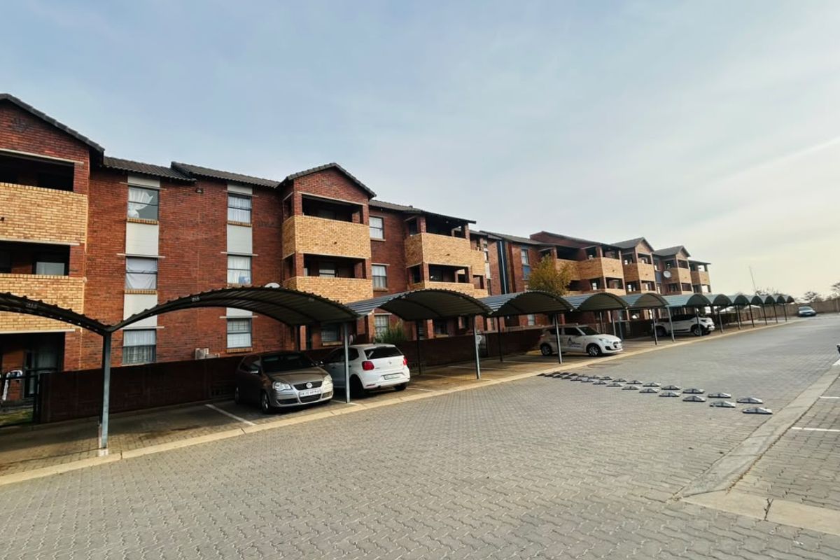 Exterior view of a multi-story brick apartment complex featuring covered parking bays and paved driveway access.
