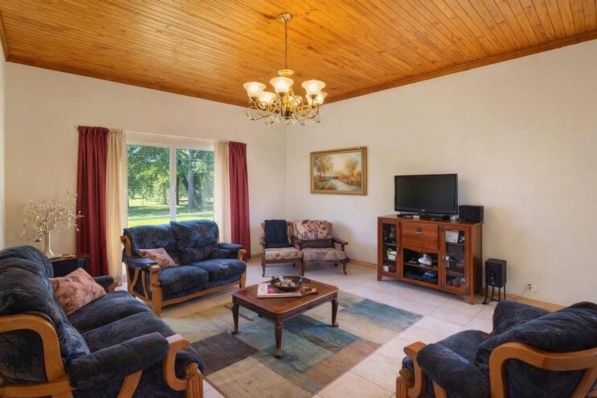 Spacious living room featuring a warm timber tongue and groove ceiling, tiled flooring, and a sliding glass door providing natural light and garden views.