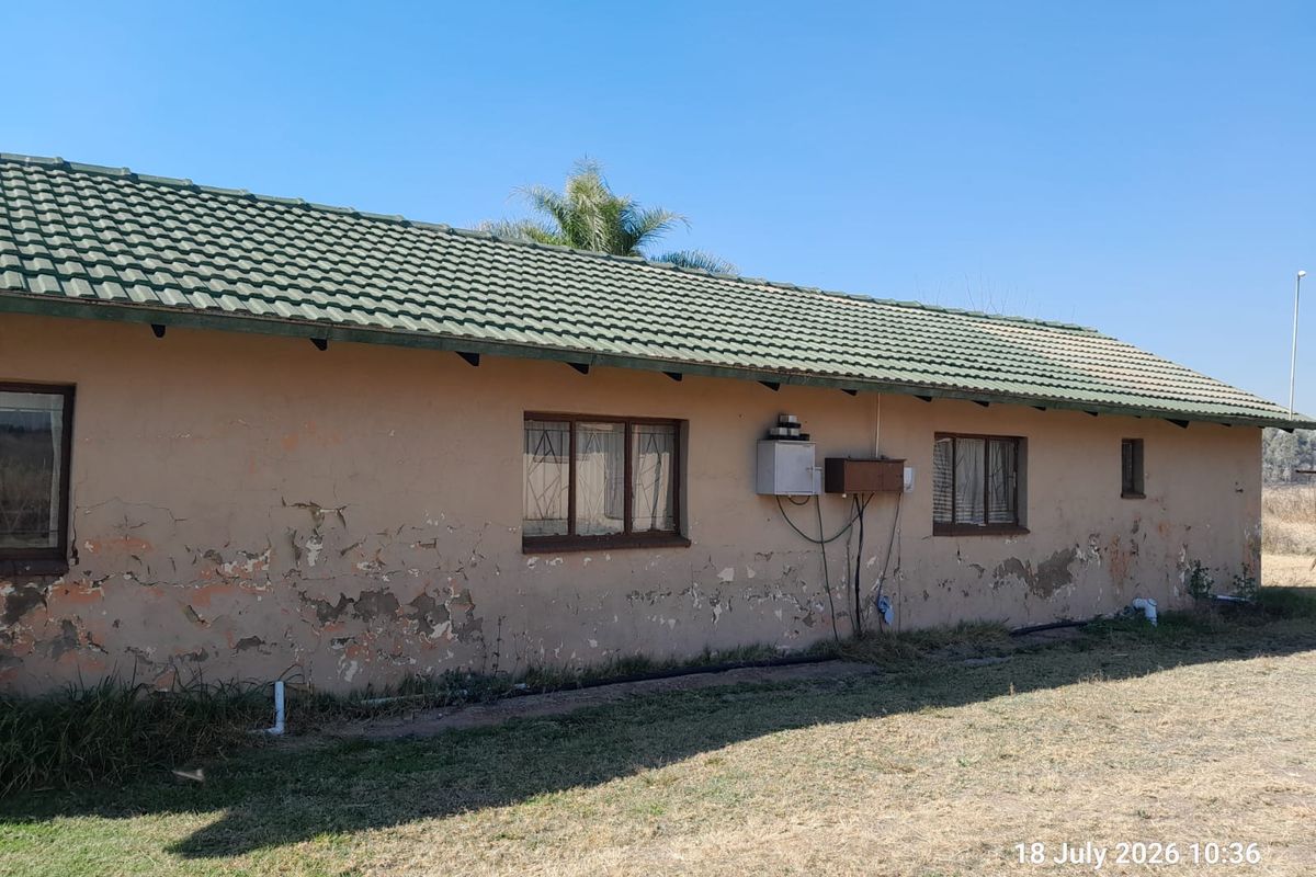 Rear exterior view of a farm building featuring a tiled roof and showing significant signs of weathered plaster and peeling paint.