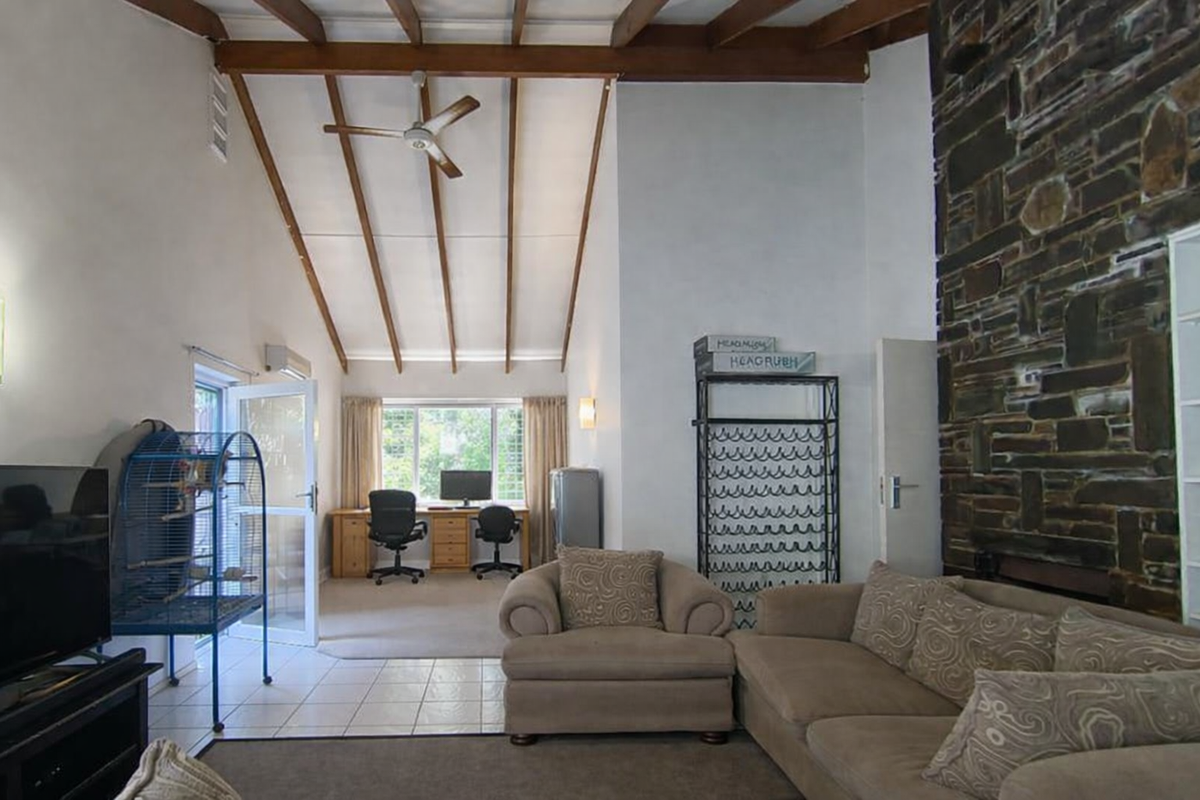 Spacious living area featuring a striking stone fireplace wall, exposed timber ceiling beams, and a seamless transition to a dedicated study or office nook.
